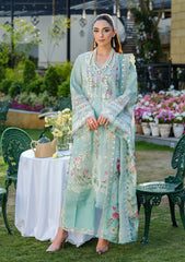 Woman in a light blue embroidered dress standing outdoors with floral decorations and greenery.