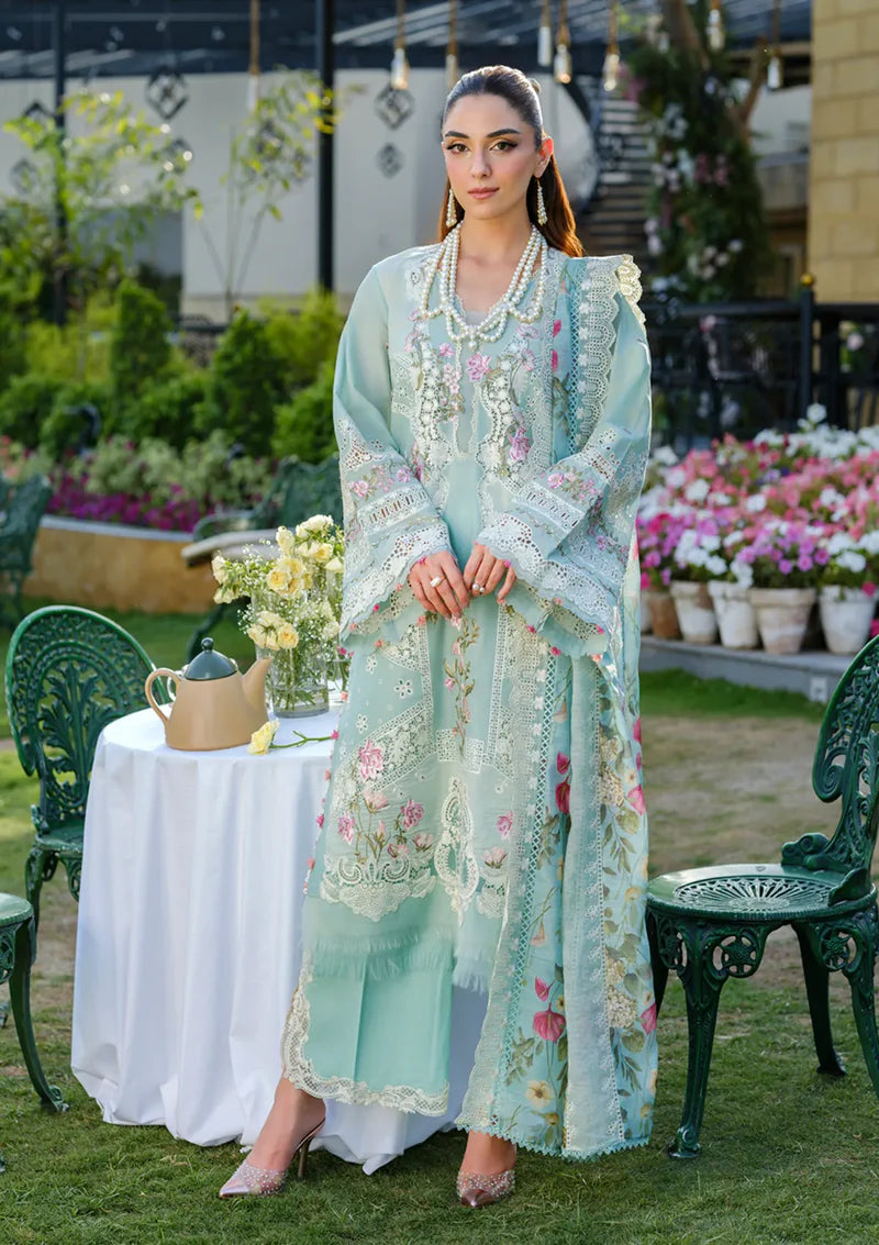Woman in a light blue embroidered dress standing outdoors with floral decorations and greenery.