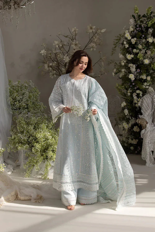 Woman in a light blue traditional outfit standing in a decorated room with flowers.