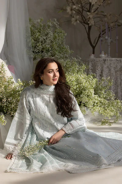 Woman in a light blue embroidered dress sitting among flowers and decorative elements.